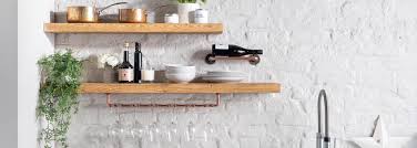 A stainless steel kitchen hood, flanked by stacked dark stained floating shelves, stands over an integrated gas cooktop. Rustic Wooden Floating Shelves And Mantel Beams