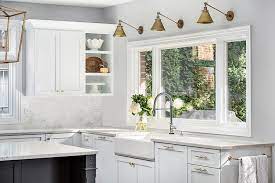 Three Antique Brass Swing Arm Sconces Are Fitted To A Light Gray Wall Above A Window Positioned Window Over Sink Sconce Above Kitchen Sink Kitchen Sink Window