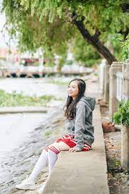 Smiling Lovely Young Asian Woman In Skirt, Hoodie And Thigh High Socks  Sitting On River Bank And Looking At Water Stock Photo, Picture and Royalty  Free Image. Image 151852170.