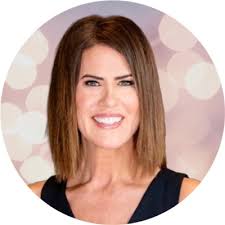 This bathroom is designed with a spacious makeup counter, crisp white  cabinetry, brass hardware, and elegant marble tile flooring.