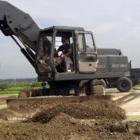 Equipment Operator Constructionman Kyle Holtzman directs Equipment Operator  Constructionman Eric Hofmans as he operates a wheel loader to move a stack  of lumber at the Ecole 5 Primary School.