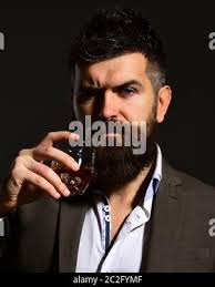 Man with serious face toasting with glass of alcohol. Connoisseur with  beard and bourbon or whiskey