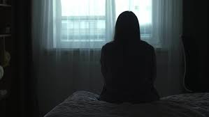 Back view Silhouette of a millennial woman sitting on bed in the dark  bedroom, depression, pain. Portrait of Unhappy sad woman sitting against  window and thinking about her life