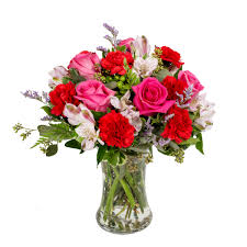The three flower stems are placed in a clear glass vase that is decorated by a florist partner with a ribbon. Marvelous Blooms Hot Pink Roses Red Carnations Light Pink Alstroemerias And Purple Accents Forest Of Flowers