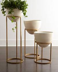Eliana Gold Planter Beverage Cooler A white ceramic planter on a wooden stand sits in a mudroom on blue cement floor tiles beneath a window dressed in a white roman shade.