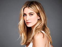 Delta goodrem, dressed in white, stands in a bare room, singing directly to camera. The Voice Mentor Delta Goodrem On Why She Ll Always Love Melbourne