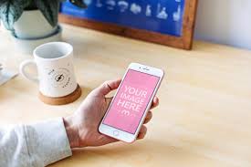 Mockup Of A Person Holding A White Iphone In Hand On A Desk Background Place Your Own Design Onto The Mobile Screen Photoshop Mockup Free Mockup Iphone Mockup
