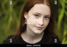 Ragazza di dodici anni dai capelli rossi con freckles in posa uno sfondo  bokeh natura Foto stock