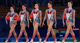 Female athletes perform expressive and acrobatic moves with the aid of handheld apparatus — a hoop, ball, pair of clubs and ribbon. W5dieulaz Sxom