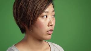 Close up of asian woman with short brown hair and a surprised expression  against a green background