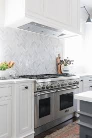 A White Wood Panel Hood Mounted To A Marble Herringbone Backsplash Is Positioned Over A Thermador Ran Cuisines Design Renovation Cuisine Backsplash Herringbone