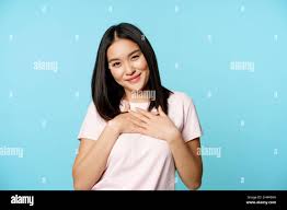 Smiling asian female model holds hands on heart, cherish smth, feeling care  and warm love feelings, standing in t-shirt over blue background Stock  Photo - Alamy