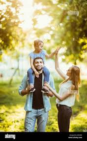 family Mom and Dad holding daughter on his back and have fun in the park  Stock Photo - Alamy