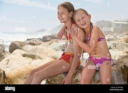 Two girls (7-9, 10-12) sitting on rock on beach Stock Photo - Alamy