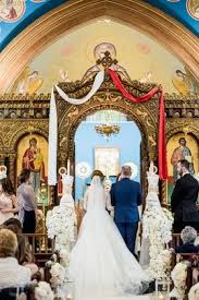 Bride And Groom At Gold Altar White And Red Sash White Flowers Orthodox Wedding Greek Wedding Traditions Greek Wedding Dresses