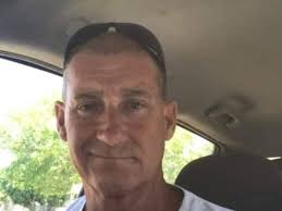 A car belonging to the Gaffney family, bogged in a sandhill near New Well  during their trip to Birdsville. Mr Gaffney kneels by the car which has  brushwood placed beneath it, as