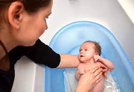 Slowly place your baby in the bath, feet first, while supporting their head. First Bath For Baby When And How To Do