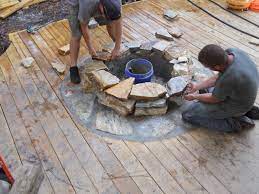 The wood has a very warm glow, with hints of red and orange. Craftsmen Constructing A Natural Stone Fire Pit On Wooden Deck With Stone Inlay Www Southernlivingou Fire Pit On Wood Deck Fire Pit Backyard Rustic Fire Pits