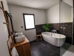 Carrelage noir intérieur de salle de bains moderne avec armoires en bois, une baignoire blanche et un évier. Salle De Bain Noire Et Blanche 16 Idees Pour Vous Inspirer Kozikaza