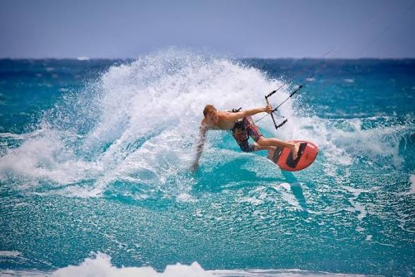Kitesurfista trazando un giro con la tabla y levantando espuma sobre el mar