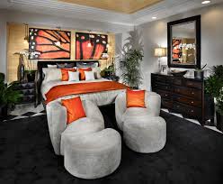 A spacious primary bedroom featuring a large classy area rug along with a stunning tray ceiling lighted by a fancy chandelier. Orange Home Accessories For Every Room Of The House