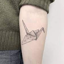 Tattoo of a pink origami crane with cherry blossom petal design on a black and orange lotus. Origami Crane Tattoo On The Inner Forearm