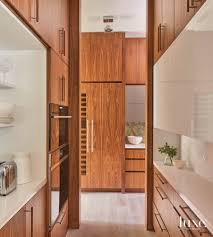A black dutch door fitted with a porthole opens to a gorgeous cottage butler's pantry equipped with an antique wood island placed against shiplap trim below a framed print and flanked by light gray cabinets finished with marble ogee countertop. Rich Wood Accents Take Center Stage In This Coastal Kitchen Luxe Interiors Design