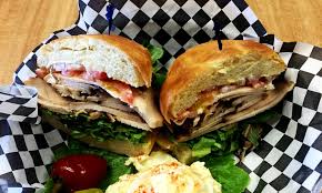 A large sandwich consisting of a long roll split lengthwise and filled with layers of various ingredients such as meat, cheese, tomatoes, lettuce, and condiments. Sandwich Shop Colorado Springs Grinder Sandwich Company Inc