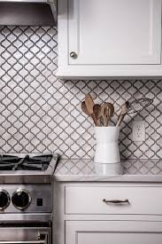 White Kitchen Cabinets Are Finished With A White Marble Countertop Located Against Kitchen Backsplash Photos Kitchen Tiles Backsplash Trendy Kitchen Backsplash