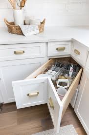 White kitchen with medium / dark hardwood flooring, light gray walls, and white window trim. Kitchen Cabinet Storage Organization Ideas Driven By Decor