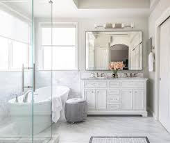 Stunning bathroom features a white lacquer dresser like vanity with glass shelf topped with gray stone fitted with a brass faucet and a brass toilet paper roll holder and an antique brass framed medicine cabinet alongside a black and white striped tile floor. White Master Bath With Gray Stool Transitional Bathroom