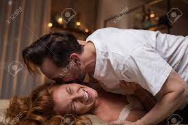 幸せな瞬間陽気な男は愛で彼の妻の耳にキスしています。女性はベッドに横たわって笑っているの写真素材・画像素材 Image 91857667