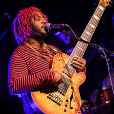 Thundercat holding his orange colored signature Ibanez 6 string bass 