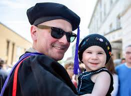 Non-traditional Student Holds Baby Daughter At His Graduation" by Stocksy  Contributor "Cara Dolan"