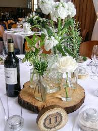 Table centrepieces of rosemary, moss in terracotta pots, cream flowers and  candles, vintage bottles and crates
