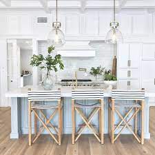 A classic white kitchen with wooden cabinets, an island table with marble countertop, pendant lights and a hardwood flooring contrasting the white elements. 25 Inspiring Coastal Kitchen Decor Ideas Shelterness