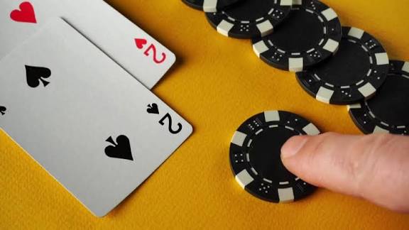 A player, seated at a table, lays out a hand of cards, either a full house or a full boat. Money and a glass lie nearby. The atmosphere creates a lively atmosphere,