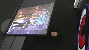 Homem aparece deitado no chão ao lado de um fliperama com arte de jogo de anime.