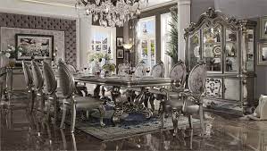 The dining table reflects highly decorative base with oversized scrolled feet, and the upholstered and tapestried chairs with the deep button tufted and nail head trim accents add classic character and represents luxurious detailing. Versailles Antique Platinum Finish Dining Set