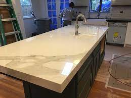 Pivot the sheet until its mitered edge lines up with the line on the counter, then press the entire edge in place, working from the outside to the inside corner. Carrara Quartz Island W Mitered Edge Detail Kitchen Interior Kitchen Remodel Mitered Edge Countertop