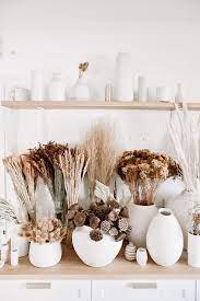 Dried white statice flower in a white vase by an empty wooden frame on a wooden floor. Dried Flower Bar Neutral Beauties Flower Bar Dried Flowers White Vases