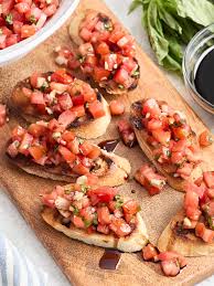 A wooden board with tomato bruschetta, fresh basil, and a drizzle of olive oil
