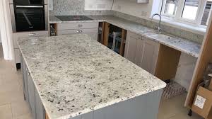 Well appointed gray kitchen features glazed white subway backsplash tiles finished with dark gray grout and framing a stainless steel kitchen hood flanked by black windows mounted above gray shaker cabinets accented with satin nickel pulls and gray granite counters located on either side of a stainless steel oven range placed on oak wood floors. Indian Granite Slab For A Modern And Trendy Kitchen