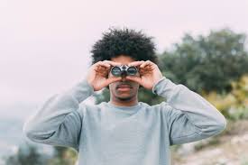 Reflected in the lenses of the binoculars are dollar signs representing money. Free Photo Man Looking Through Binoculars