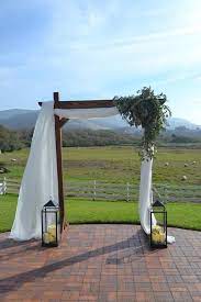 Simple And Rustic Wood Arch Draped With Chiffon And Asymmetrical Greenery Decor Fleurish Floral Designs Wood Wedding Arches Greenery Decor Herb Wedding