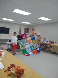 Debra Barlow Hardy showing a t- shirt quilt she made for her grandson at  the October council meeting and a group of mhv at the State Veterans home  presenting donations from the