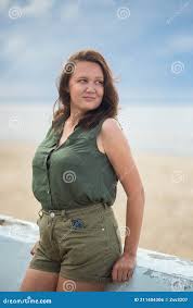 Beautiful Busty Curvy Woman in Olive Blouse and Shorts Posing Near the Sea  in the Atmospheric Cloudy Weather Stock Photo 