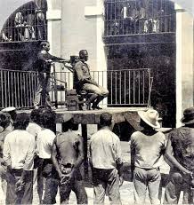 This haunting photograph captures a man moments before his execution by a  device known as the garrote—a brutal method of capital punishment that  persisted for centuries. The condemned would be seated, his