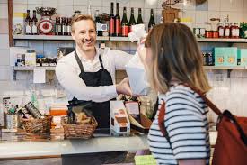 Wholesalers buy it for $2 and then sell it to retailers for $4. Male Sales Clerk Smiling While Handing Over Bag To Customer At Counter In Store Stockphoto