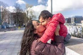 Liebevolle Frau küsst ihre Tochter, die auf einer Stützmauer in der Stadt  sitzt, lizenzfreies Stockfoto